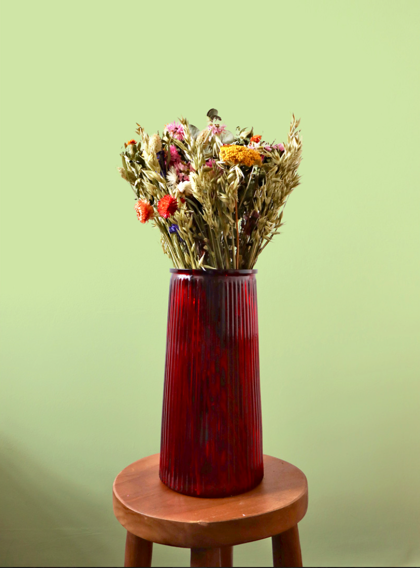 Red vase with dried flowers on a wooden stool against a green background