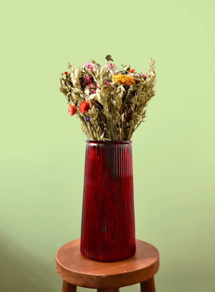 Red vase with dried flowers on a wooden stool against a green background