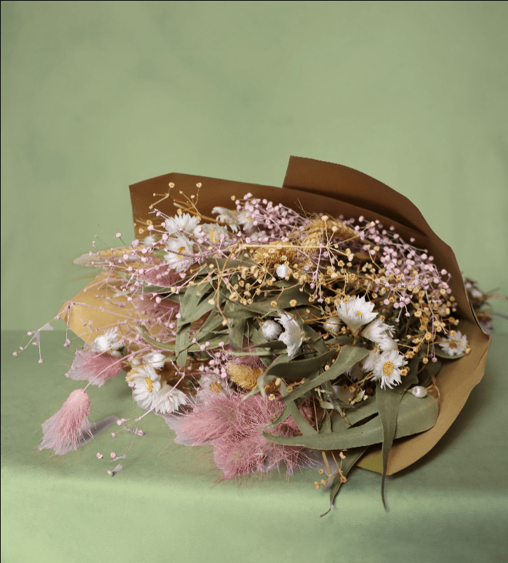 Bouquet of dried flowers wrapped in brown paper on a green background