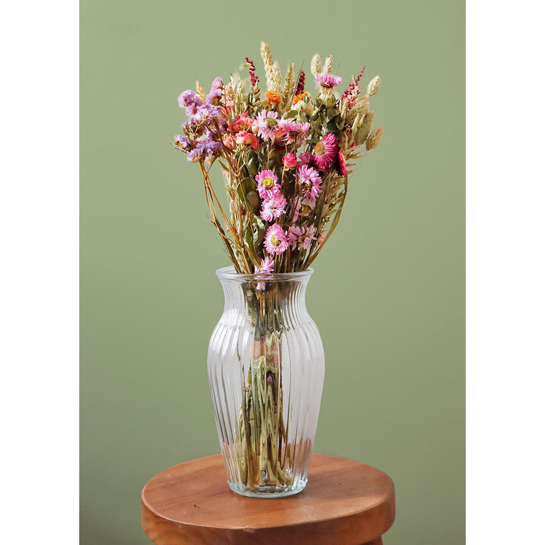 Clear glass vase with dried flowers on a wooden surface against a green background