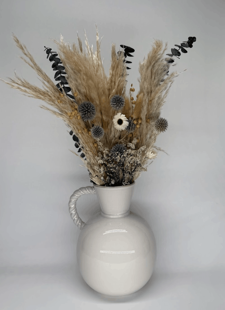 Dried flower bouquet in silver grey and blue tones with pampas grass and globe thistles in a white ceramic vase on a grey background