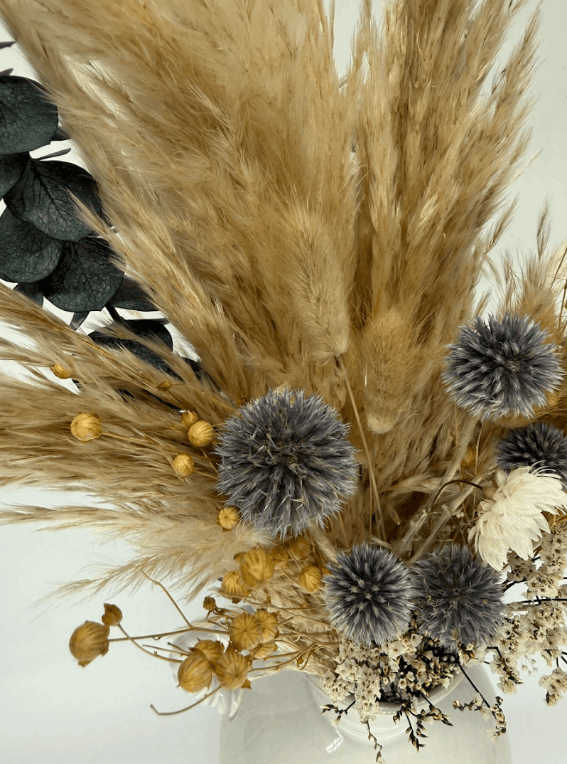 Top-down view of dried flower bouquet with pampas grass, blue globe thistles, and dark eucalyptus leaves on a white background