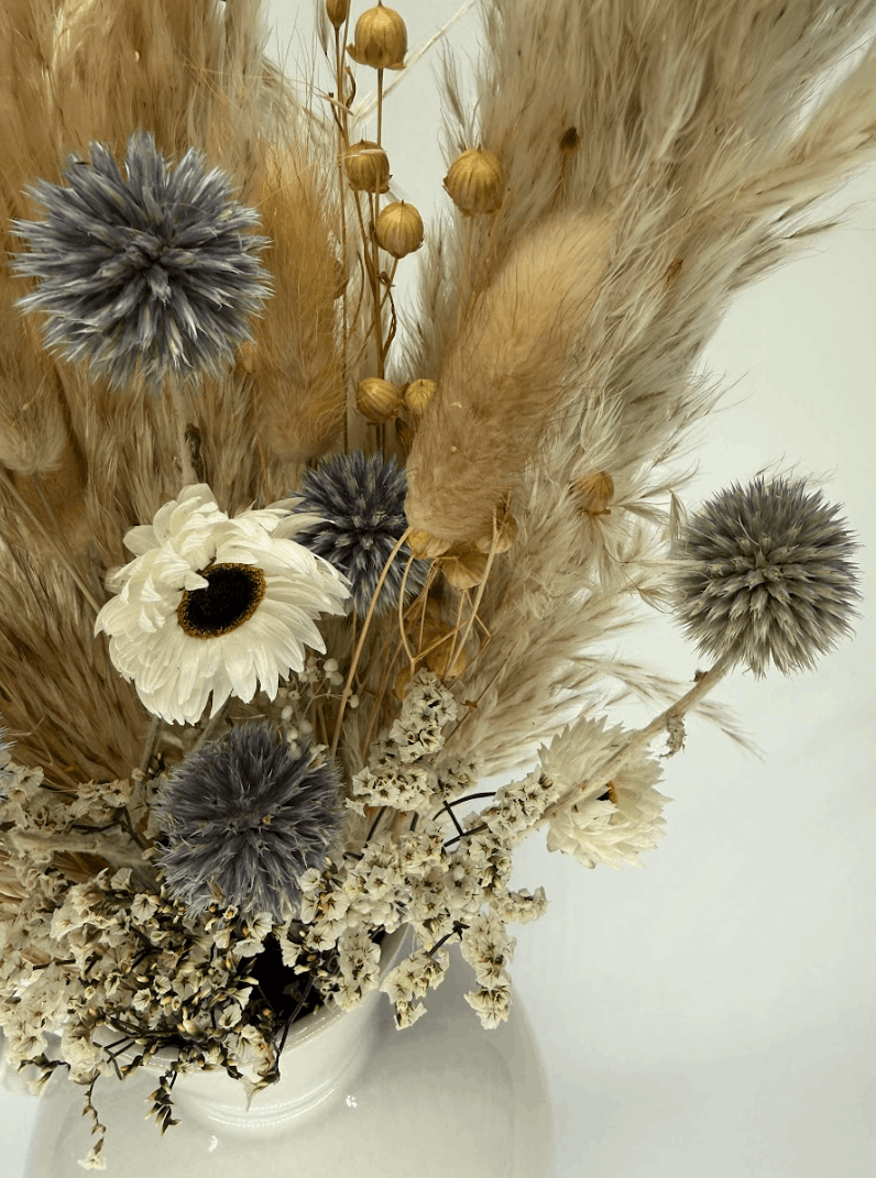 Close-up of dried flower bouquet with blue globe thistles, pampas grass, and white dried flowers in a white ceramic vase