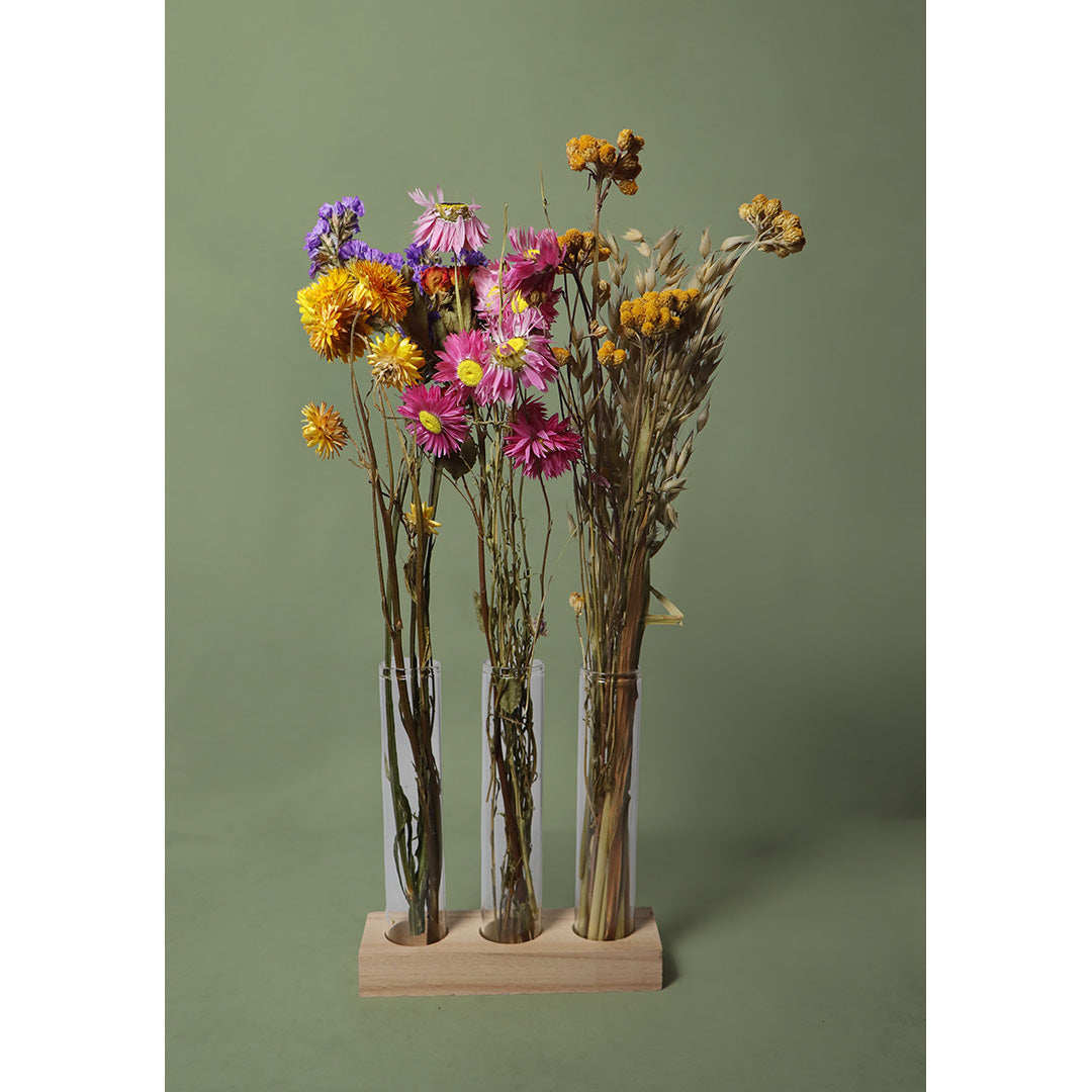 Three glass vases with dried flowers on a wooden stand against a green background