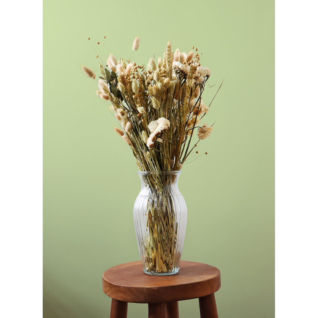 Clear glass vase with dried flowers on a wooden stool against a green background