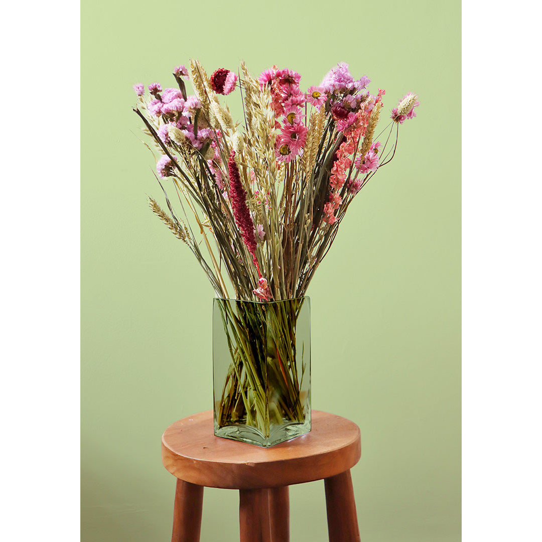 Glass vase with pink and gold flowers on a wooden stool against a green background
