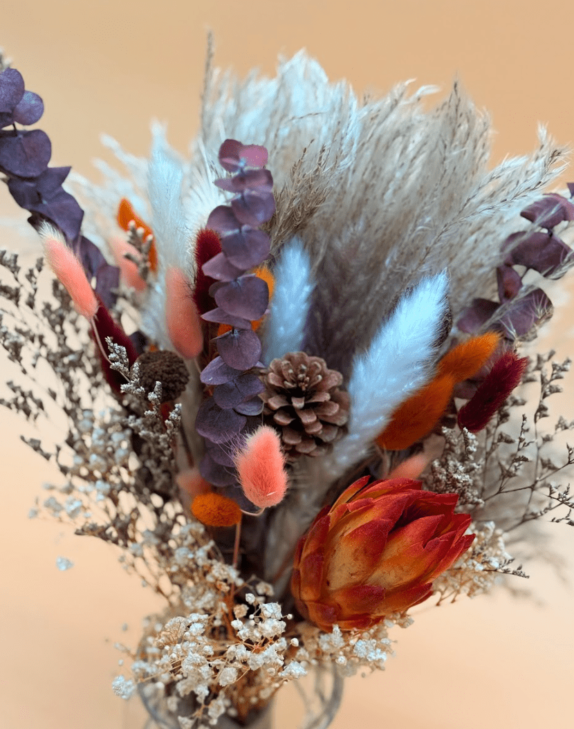Dried floral arrangement with orange, purple, and white flowers on a beige background