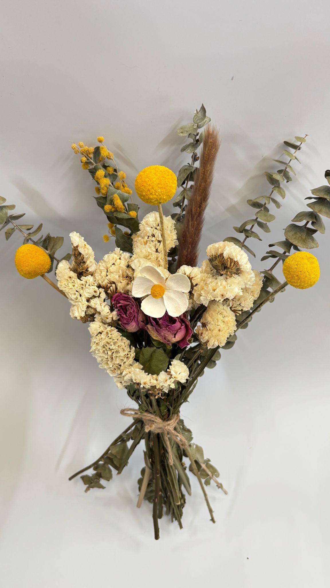 Bouquet of dried flowers with yellow balls and green leaves on a white background