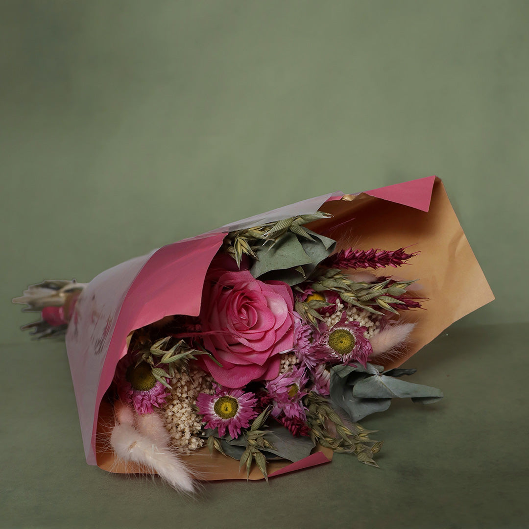 Bouquet of flowers wrapped in pink paper on a green background