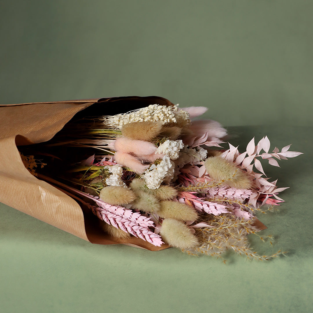 Bouquet of dried flowers wrapped in brown paper on a green background