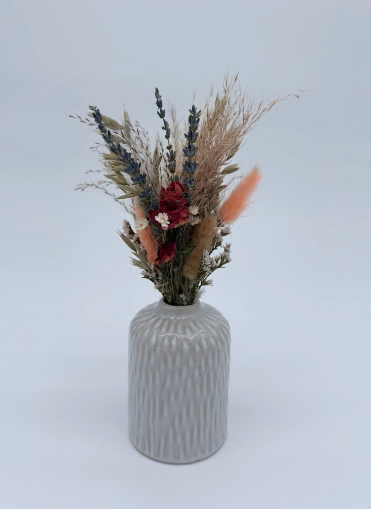 White textured vase with dried flowers on a light surface and white background