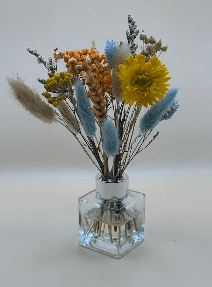 Clear glass vase with dried flowers including yellow and blue elements on a white background