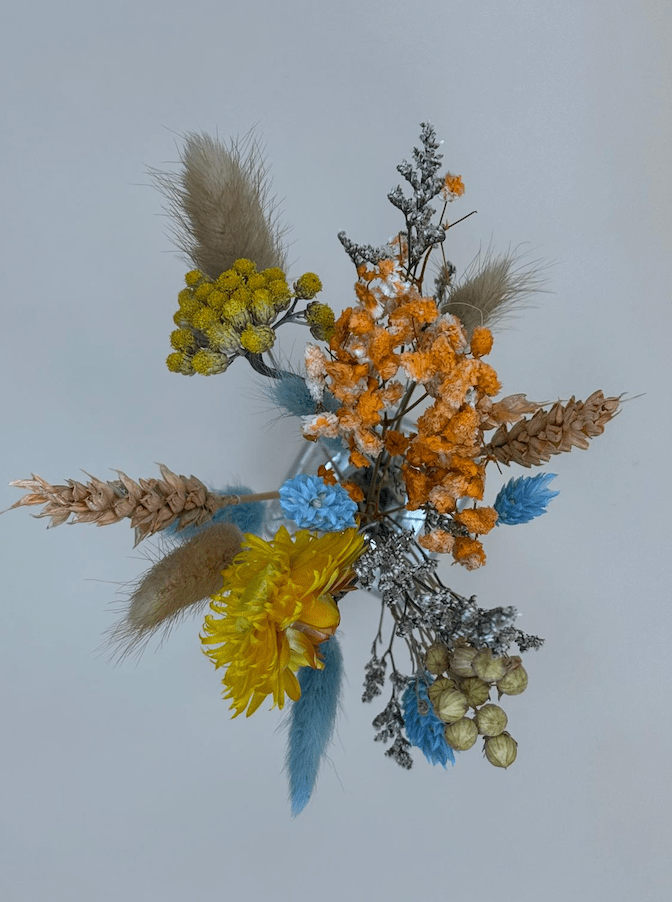 Bouquet of dried flowers with orange, yellow, and blue elements on a light gray background