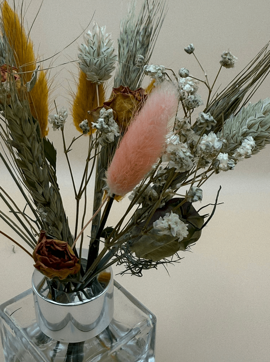 Decorative arrangement of dried flowers and a pink bunny tail in a silver vase on a light background
