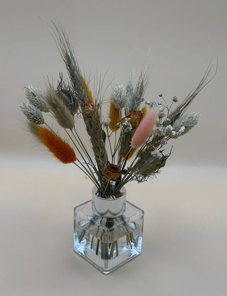 Clear glass vase with dried flowers on a light gray background