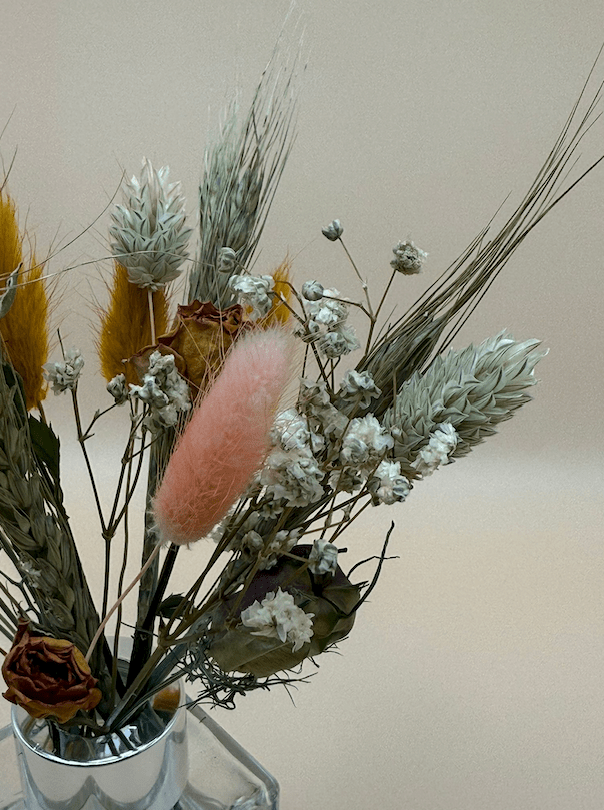 Decorative arrangement of dried flowers and a pink decorative item against a plain background