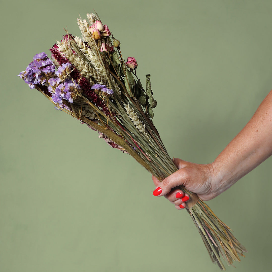 Hand holding a bouquet of dried flowers against a green background