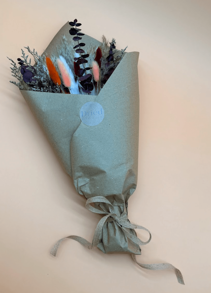 Bouquet of flowers wrapped in light green paper with a decorative label on a beige background