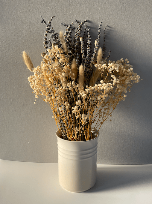 Bouquet of dried flowers in a white vase against a plain wall