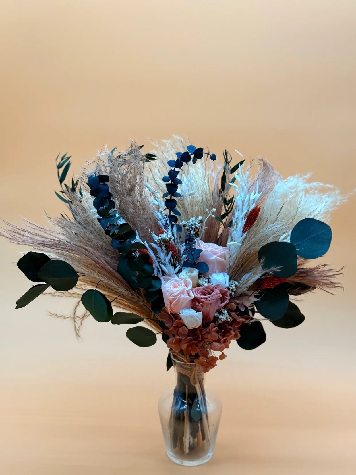 Bouquet of dried flowers in a clear vase on a beige background