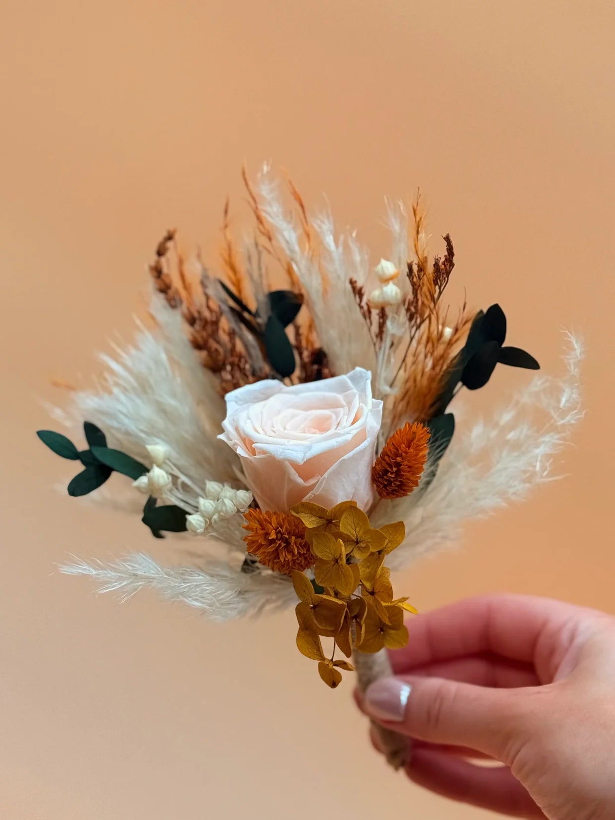 Hand holding a small bouquet of dried flowers against an orange background