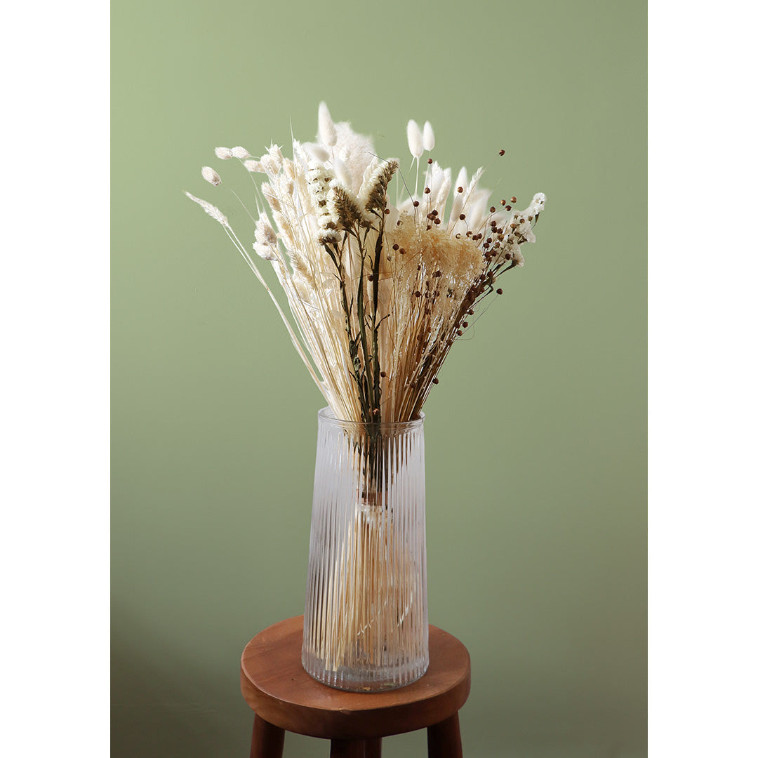 White fluffy dried blooms bouquet in a glass vase on a small round wooden table