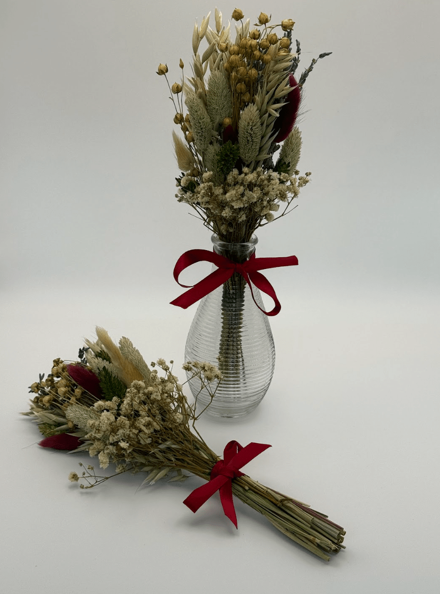 Clear glass vase with dried flowers and a red ribbon on a white background