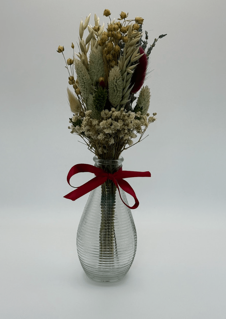 Clear glass vase with dried flowers and a red ribbon on a white background