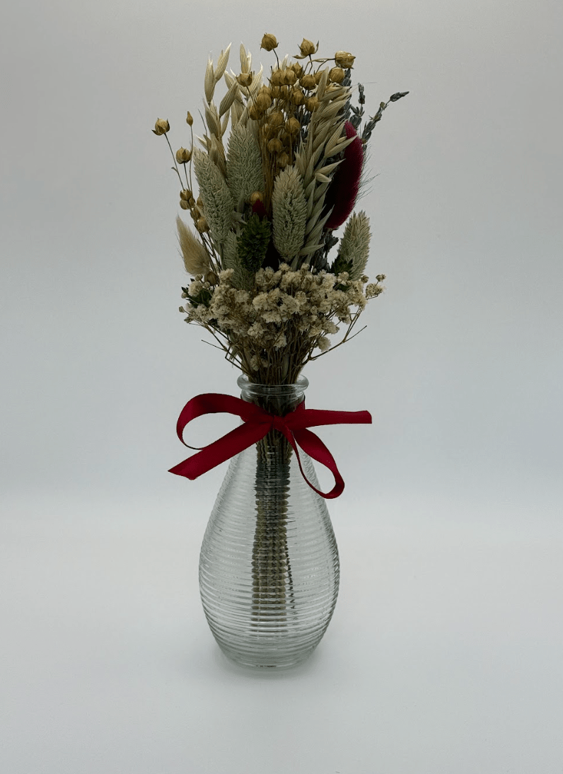 Clear glass vase with dried flowers and a red ribbon on a white background