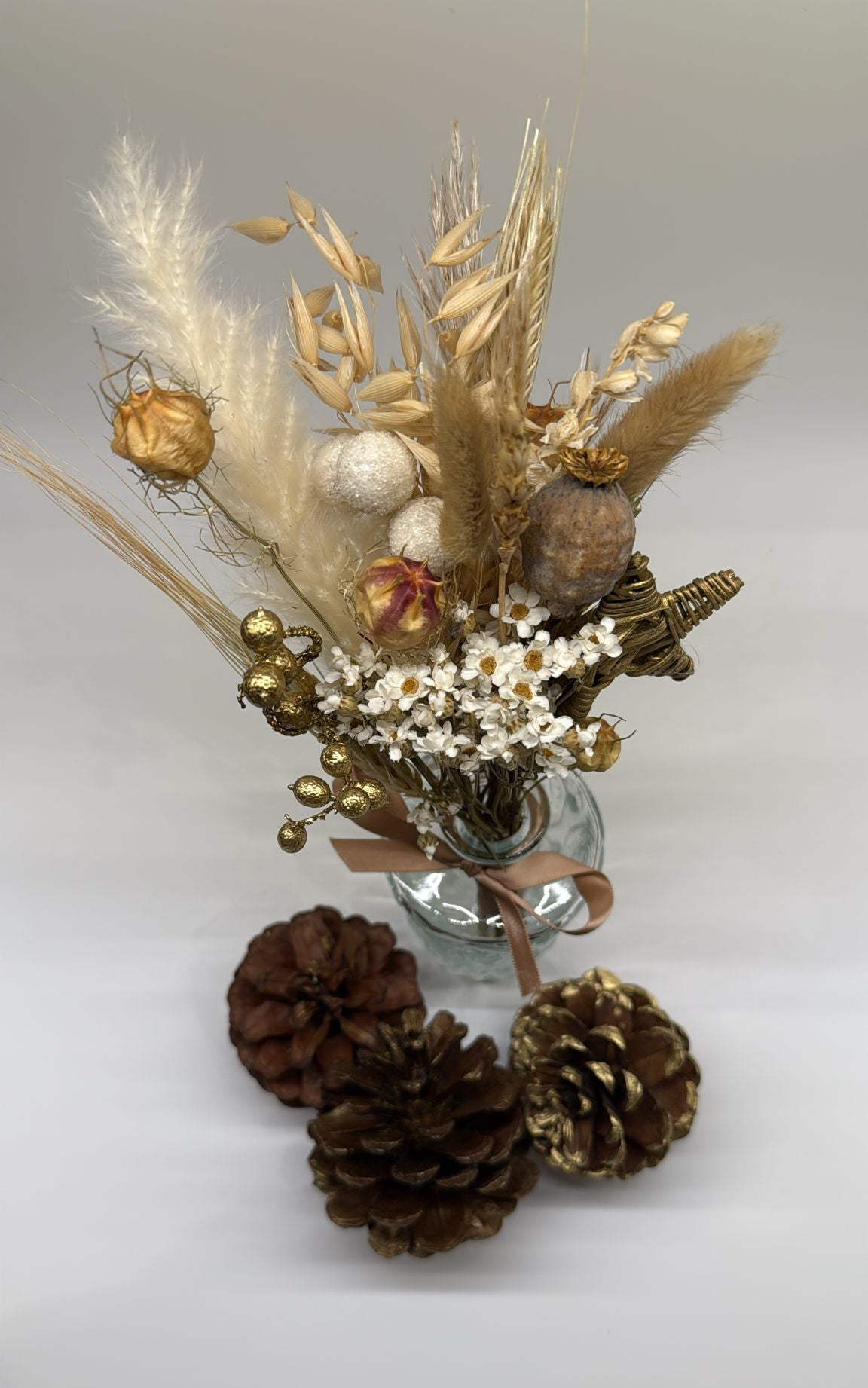 Decorative arrangement with dried flowers, pinecones, and a glass vase on a light background