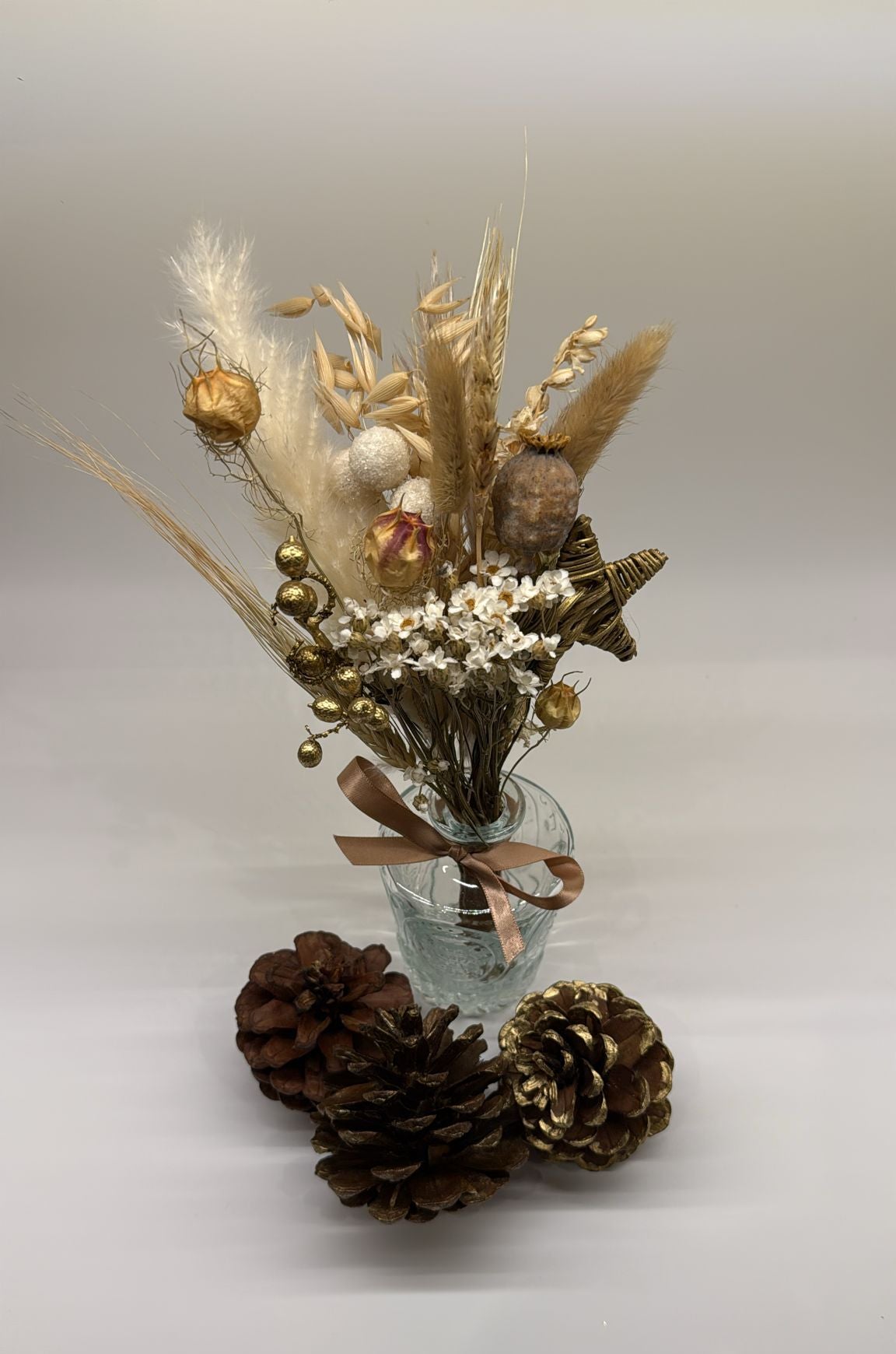 Decorative arrangement with flowers, pinecones, and a small vase on a light background