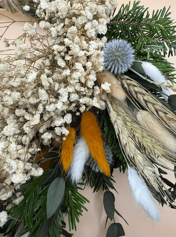 Decorative arrangement with dried flowers, greenery, and feathers on a neutral background