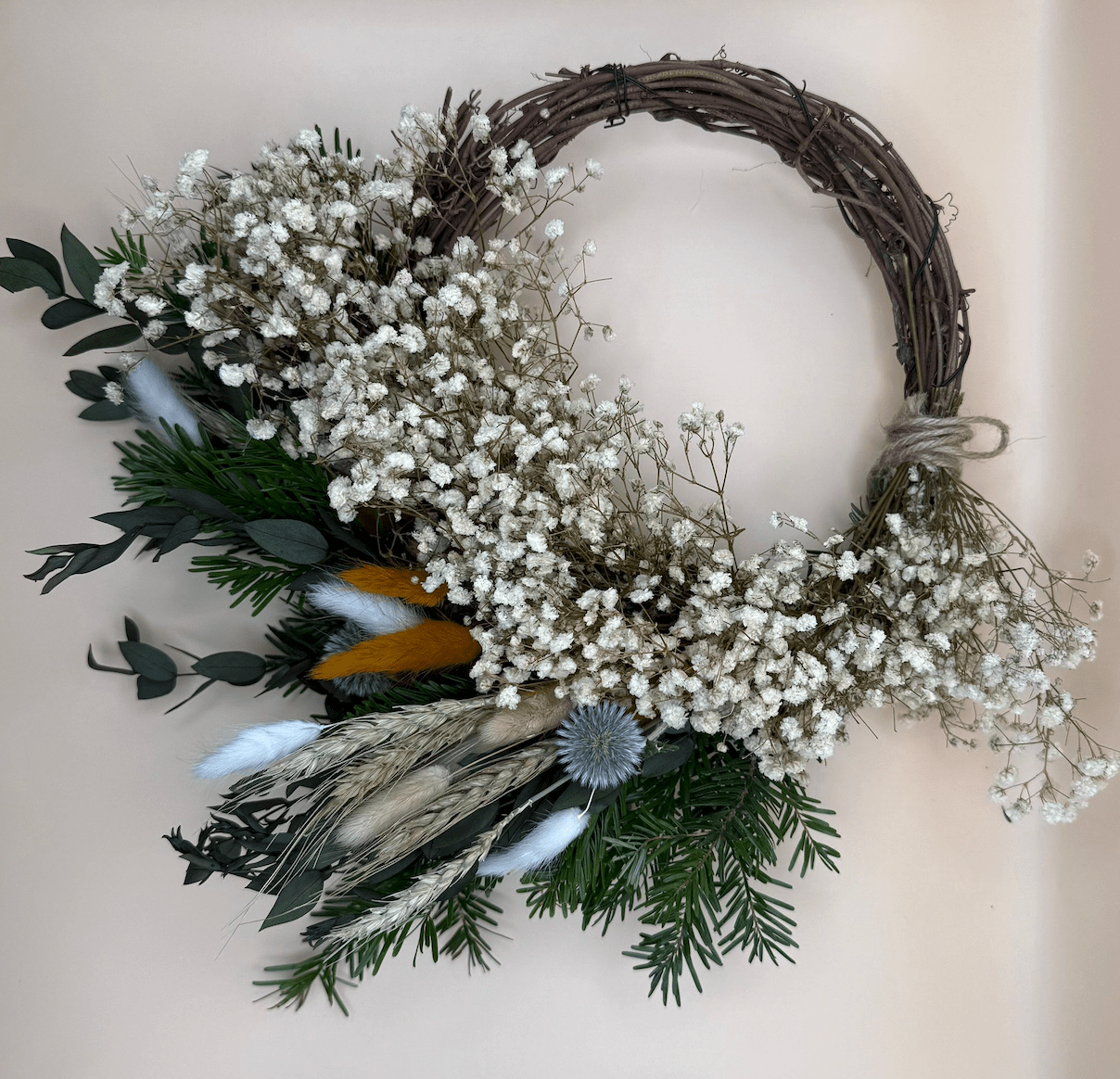 Decorative wreath with white flowers, green leaves, and feathers on a neutral background