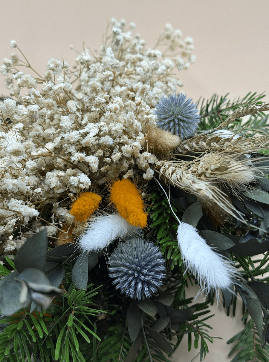 Decorative arrangement of dried flowers, greenery, and feathers on a neutral background