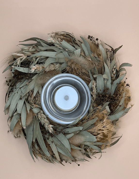 Decorative wreath with a candle holder featuring green and brown leaves on a beige background