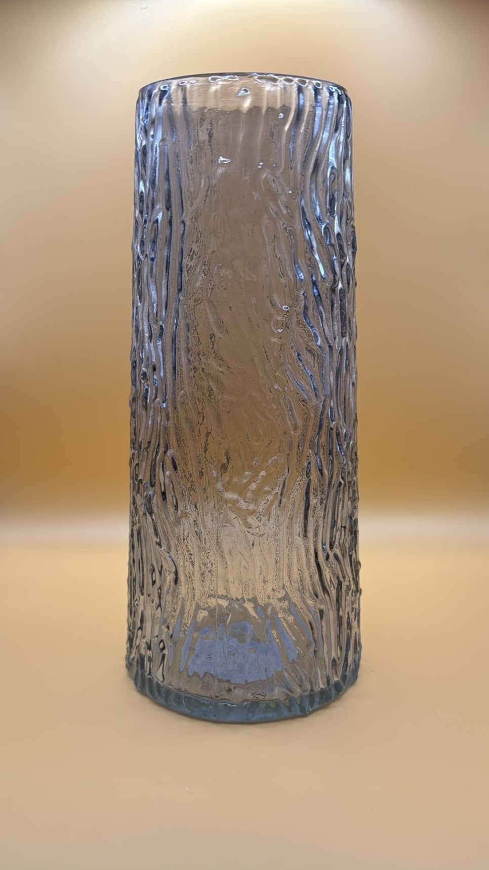 Cylindrical glass vase with textured surface on a beige background