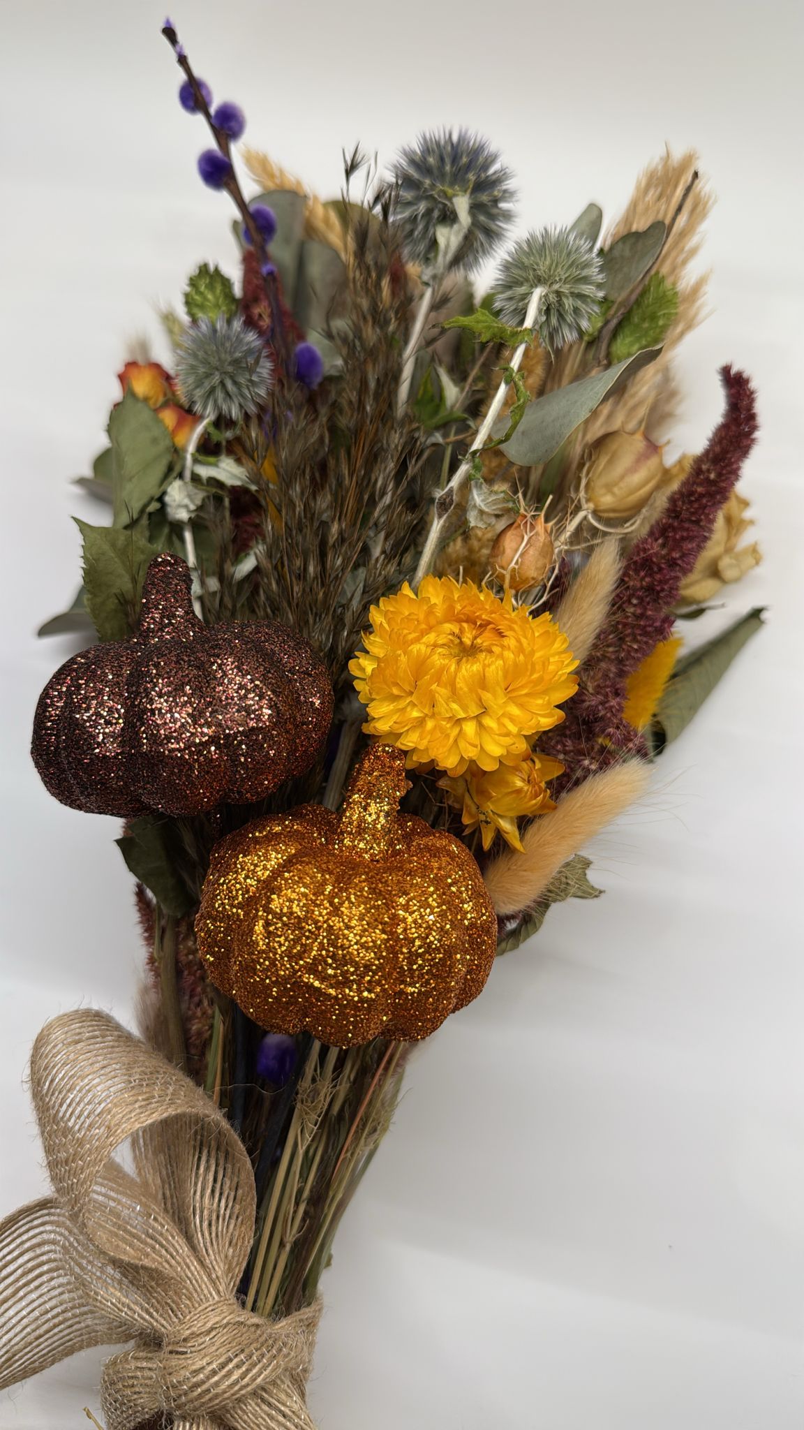 Bouquet with glittery pumpkins, yellow flowers, and dried foliage on a white background