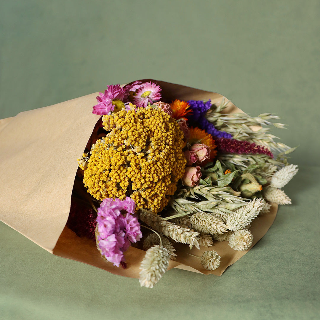 Bouquet of dried flowers wrapped in brown paper on a green background