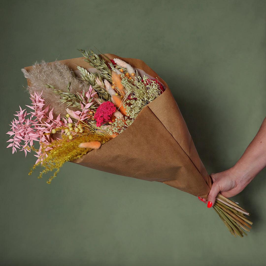 Bouquet of dried flowers wrapped in brown paper held against a green background