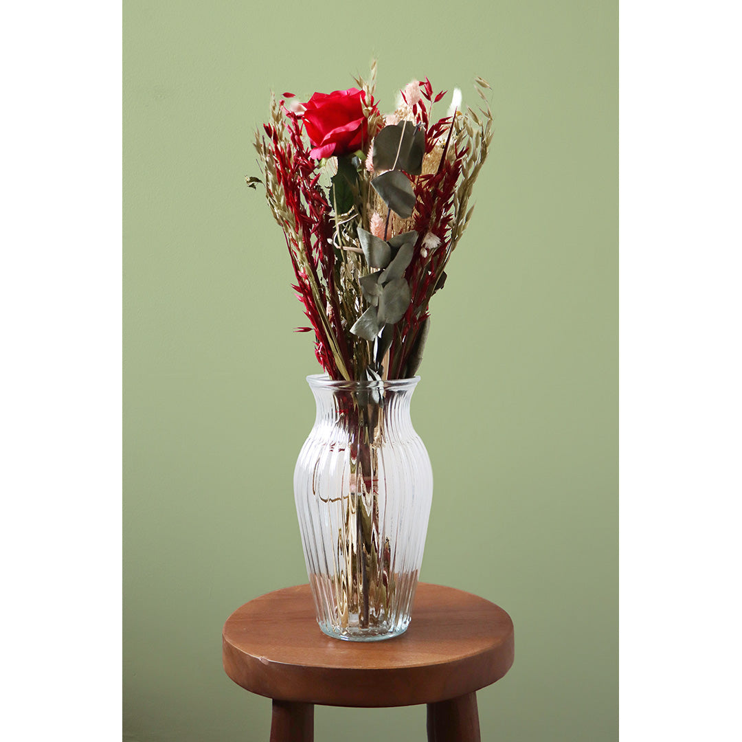 Clear glass vase with red and green flowers on a wooden stool against a green background