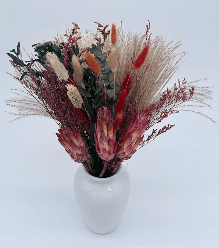 Bouquet of dried flowers in a white vase on a light gray background