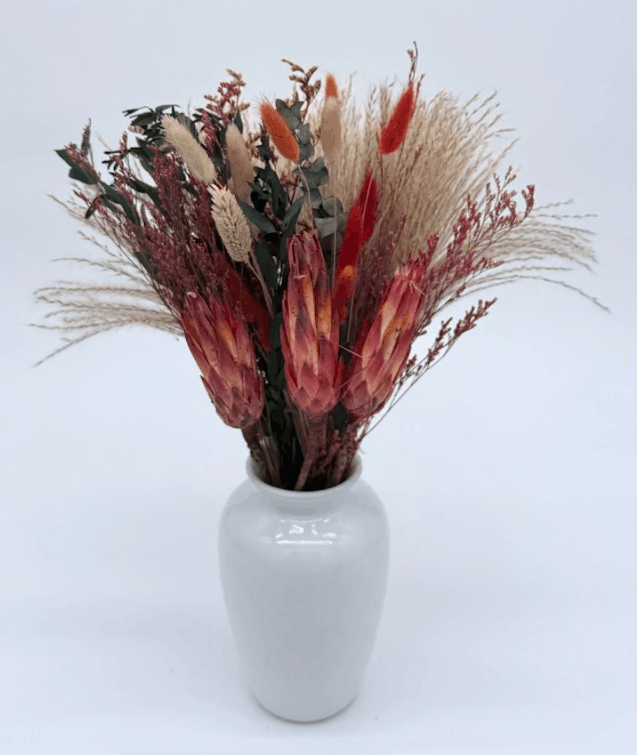 Bouquet of dried flowers in a white vase on a light gray background