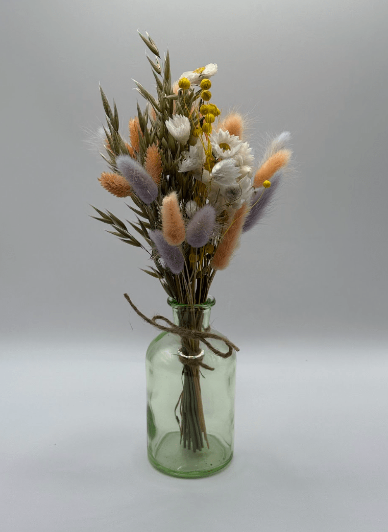 Bouquet of dried flowers in a green glass bottle on a gray background