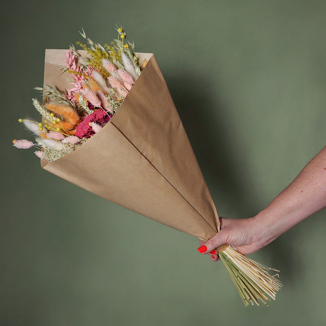 Bouquet of dried flowers wrapped in brown paper held against a green background