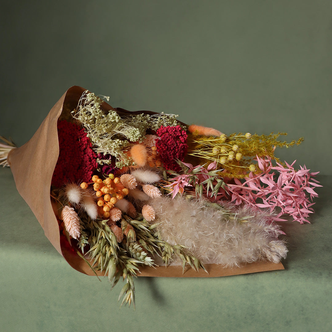 Bouquet of dried flowers wrapped in brown paper on a green background
