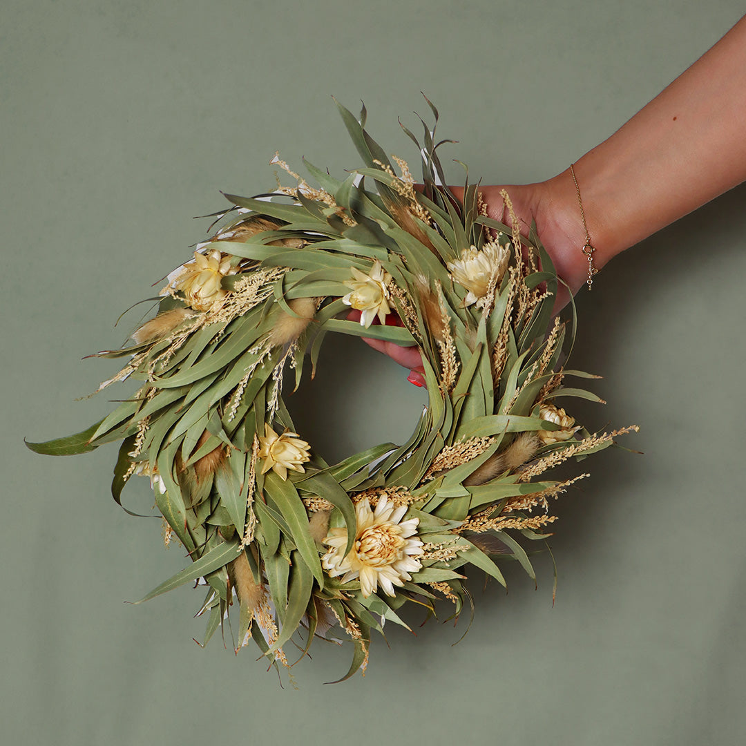 Hand holding a green floral wreath against a green background
