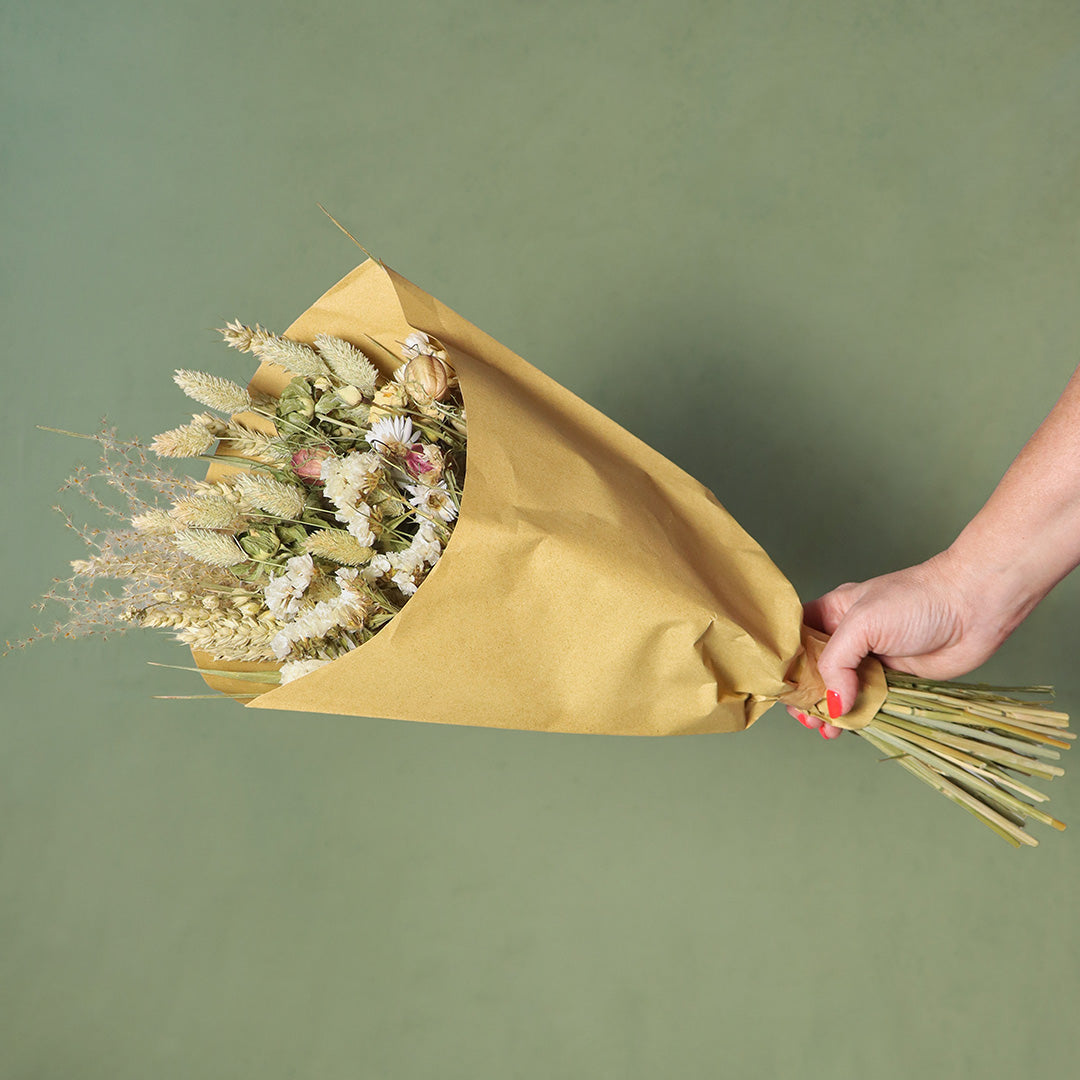 Bouquet of dried flowers wrapped in yellow paper held by a hand on a green background
