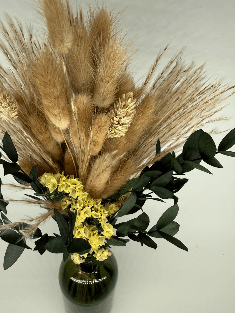 Dried flower arrangement with pampas grass, bunny tails, yellow flowers, and eucalyptus in a green vase on a dark background