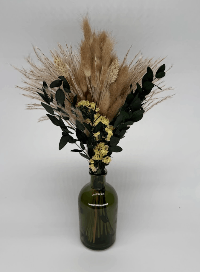 Side view of dried flower arrangement with pampas grass, eucalyptus, and yellow flowers in a green bottle vase on a white background