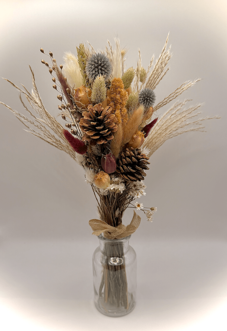 Bouquet of dried flowers and pinecones in a clear glass vase on a light gray background